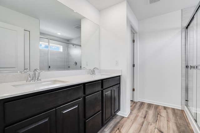 bathroom featuring a sink, double vanity, a stall shower, and wood finished floors