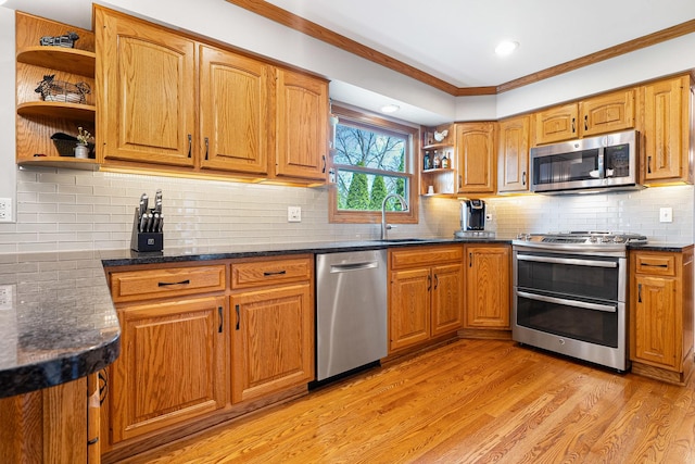 kitchen featuring crown molding, open shelves, appliances with stainless steel finishes, a sink, and light wood-style flooring