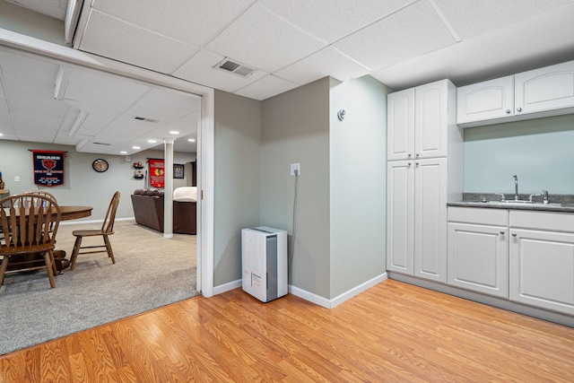kitchen featuring visible vents, a drop ceiling, white cabinetry, a sink, and light wood-style flooring