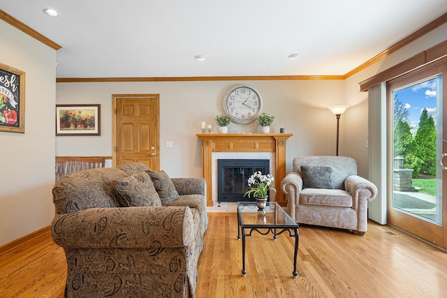 living room with crown molding, recessed lighting, a glass covered fireplace, and light wood-type flooring