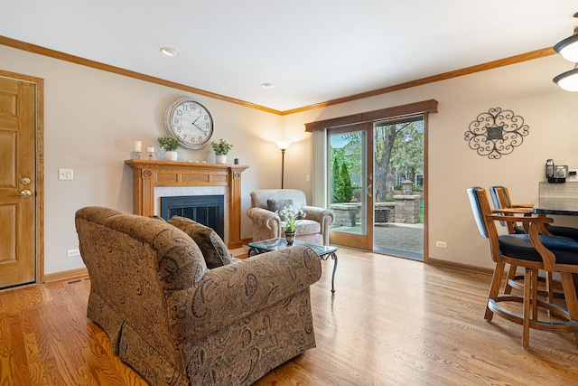 living area with crown molding, a glass covered fireplace, baseboards, recessed lighting, and light wood finished floors