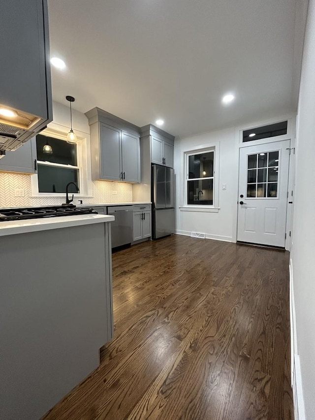 kitchen featuring gray cabinets, backsplash, light countertops, stainless steel appliances, and dark wood-type flooring