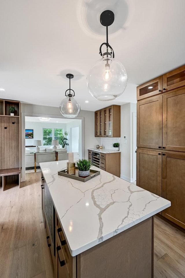 kitchen featuring a center island, hanging light fixtures, light wood-type flooring, beverage cooler, and glass insert cabinets