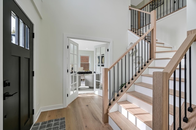 foyer entrance featuring stairs, wood finished floors, baseboards, a high ceiling, and french doors