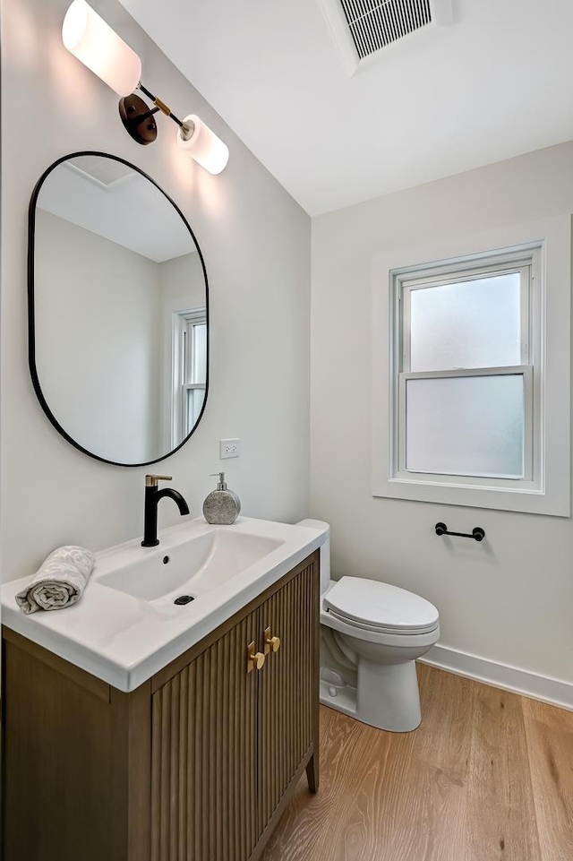 half bath featuring visible vents, wood finished floors, vanity, baseboards, and toilet