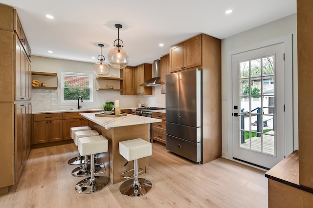 kitchen featuring wall chimney range hood, open shelves, brown cabinets, and freestanding refrigerator