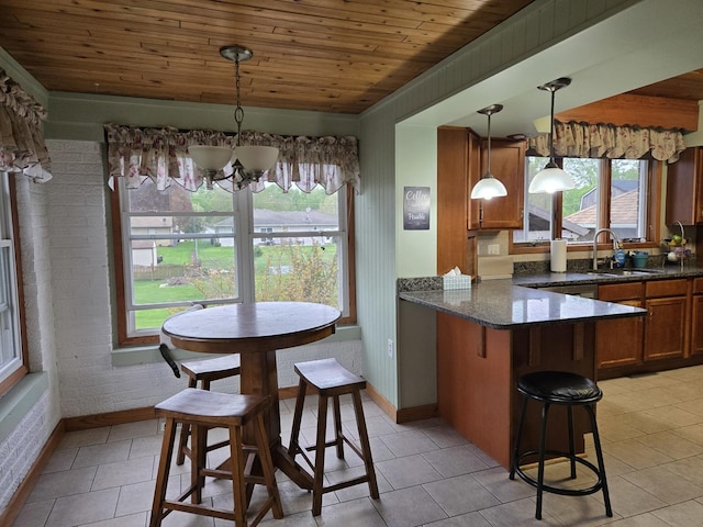 kitchen featuring light tile patterned flooring, a sink, brown cabinetry, a peninsula, and wooden ceiling
