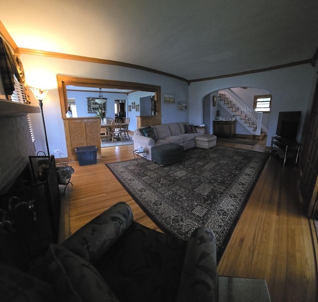 living room featuring arched walkways, stairs, wood finished floors, and ornamental molding