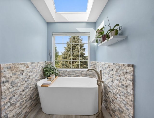 full bath featuring a skylight, tile walls, a freestanding tub, and wainscoting