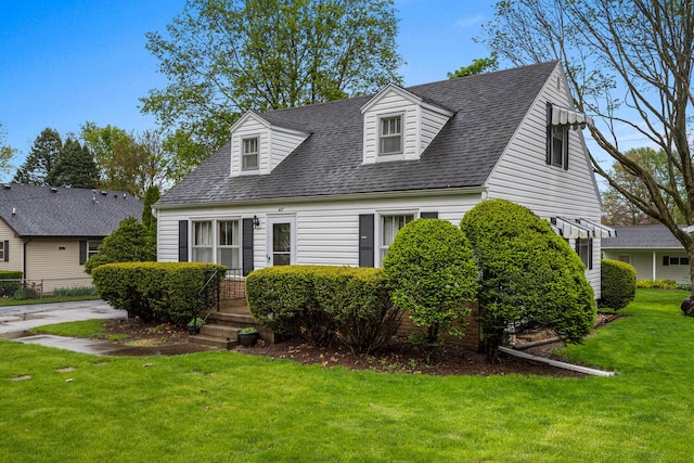 cape cod-style house featuring roof with shingles and a front yard