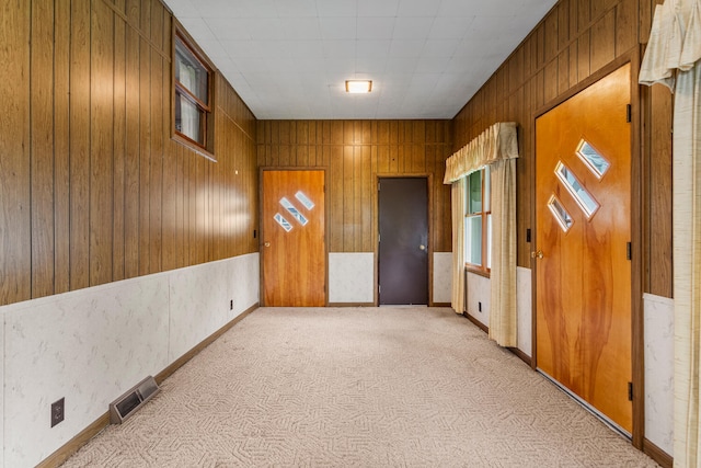 spare room with wooden walls, visible vents, and light carpet