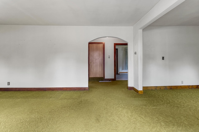 carpeted spare room featuring arched walkways and baseboards