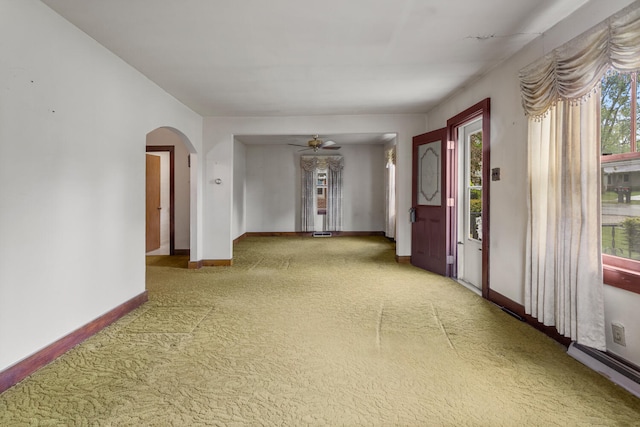 carpeted spare room with arched walkways, baseboards, and ceiling fan