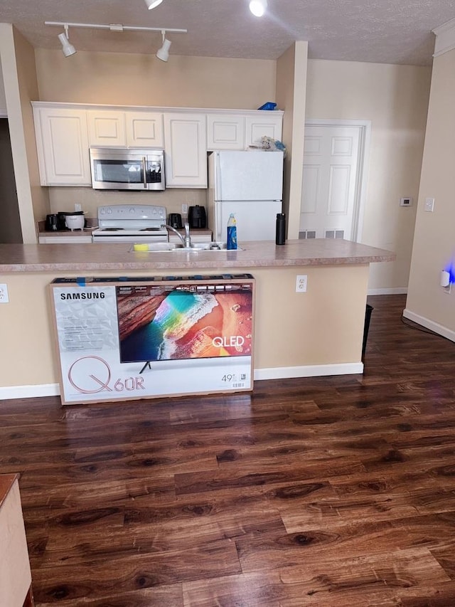kitchen with a sink, white appliances, track lighting, dark wood finished floors, and white cabinetry