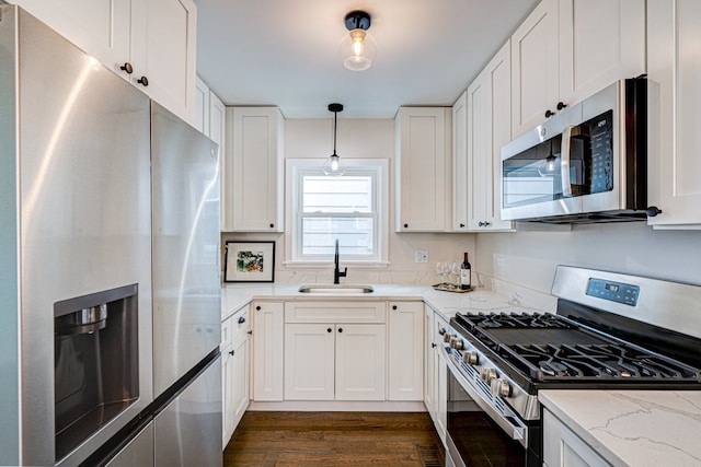 kitchen with white cabinets, light stone counters, a sink, stainless steel appliances, and dark wood-type flooring