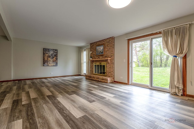 unfurnished living room featuring baseboards, a brick fireplace, wood finished floors, and visible vents