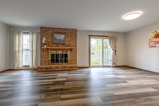 unfurnished living room with a brick fireplace, baseboards, and wood finished floors