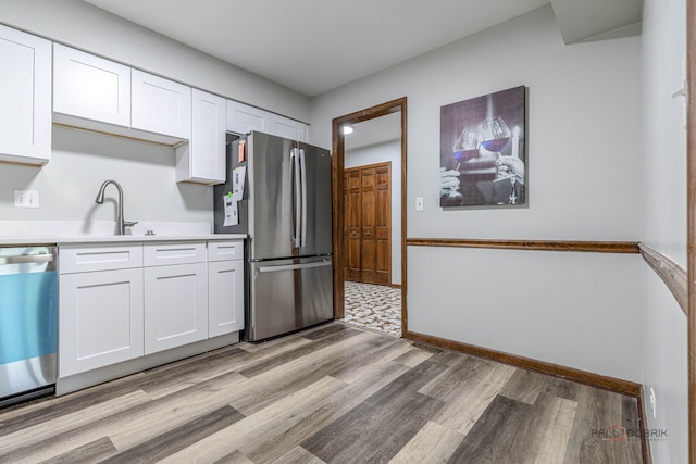 kitchen with a sink, white cabinets, stainless steel appliances, and light wood-type flooring