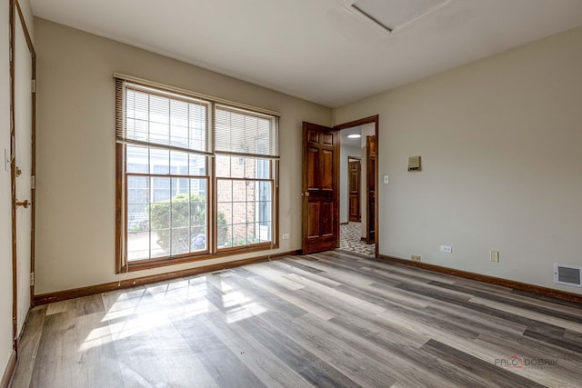 unfurnished room featuring baseboards, light wood-style flooring, a wealth of natural light, and visible vents