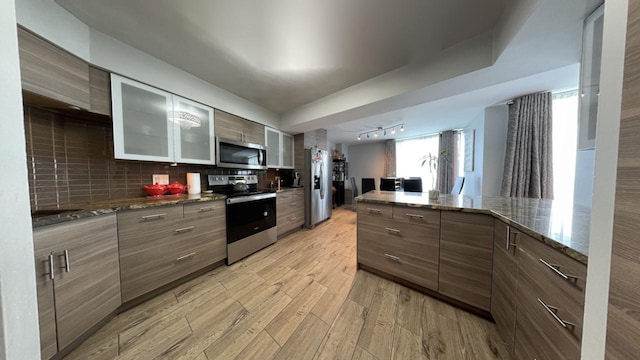 kitchen with appliances with stainless steel finishes, track lighting, decorative backsplash, light wood-type flooring, and glass insert cabinets