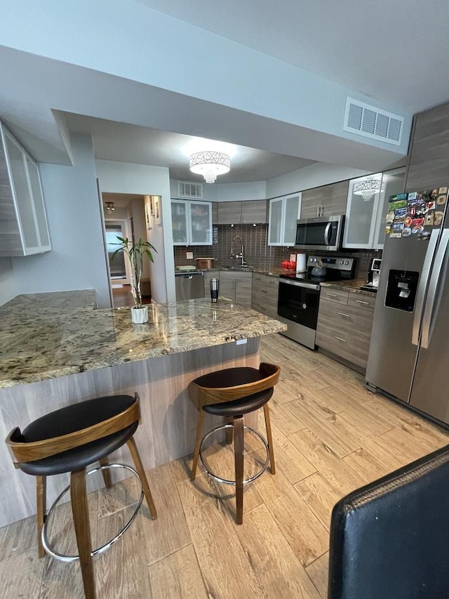 kitchen featuring a breakfast bar area, visible vents, glass insert cabinets, stainless steel appliances, and light wood-style flooring