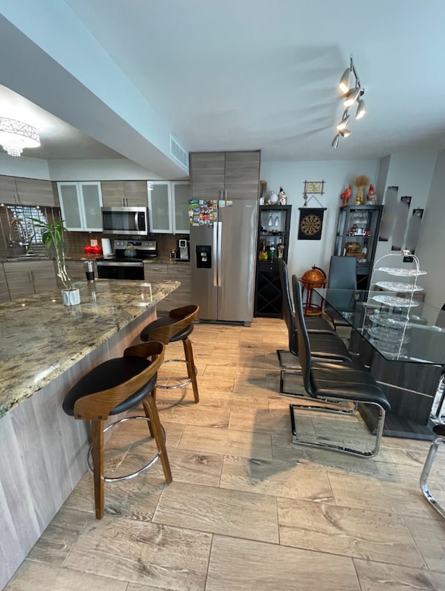 kitchen featuring glass insert cabinets, a kitchen breakfast bar, visible vents, light wood-style floors, and stainless steel appliances