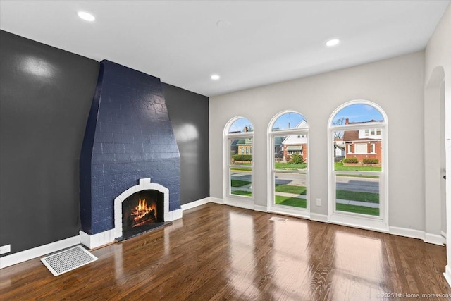 unfurnished living room with baseboards, visible vents, wood finished floors, and a fireplace