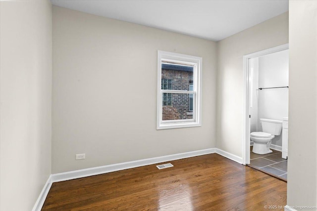 unfurnished bedroom featuring baseboards, visible vents, ensuite bathroom, and dark wood-type flooring