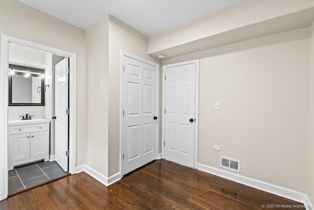corridor featuring baseboards, visible vents, dark wood-style floors, and a sink