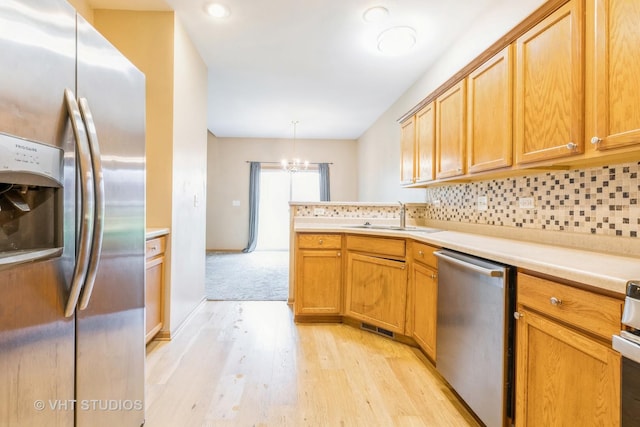kitchen featuring appliances with stainless steel finishes, a sink, light wood-style floors, a chandelier, and decorative backsplash