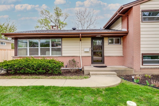 view of exterior entry featuring a lawn and brick siding