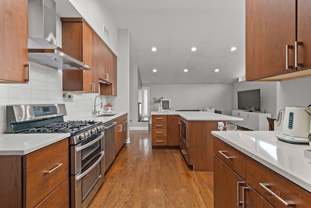 kitchen featuring wall chimney range hood, recessed lighting, a sink, dark wood finished floors, and stainless steel appliances