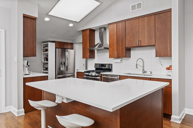 kitchen featuring wall chimney range hood, wood finished floors, a sink, lofted ceiling with skylight, and stainless steel appliances