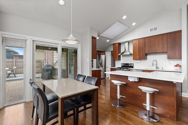 kitchen with wall chimney range hood, light countertops, a sink, dark wood finished floors, and stainless steel appliances