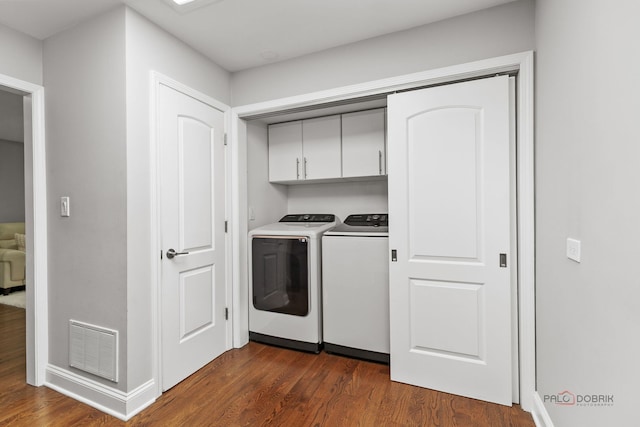 laundry area featuring washing machine and clothes dryer, dark wood finished floors, cabinet space, and visible vents