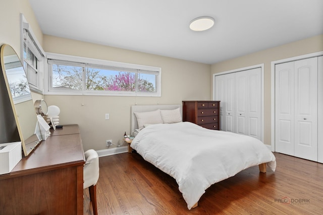 bedroom featuring baseboards, multiple closets, and wood finished floors