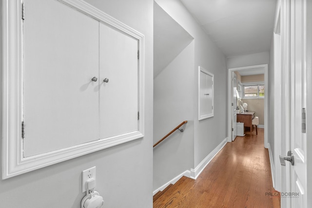 hall with baseboards, wood finished floors, and an upstairs landing