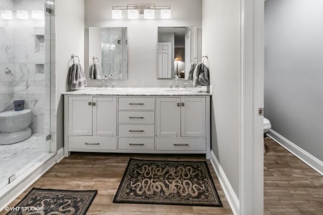 bathroom with wood finished floors, a sink, a stall shower, and toilet
