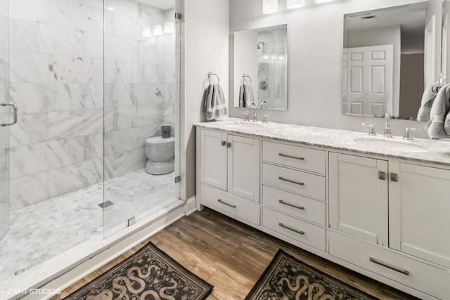 bathroom with a sink, a stall shower, double vanity, and wood finished floors