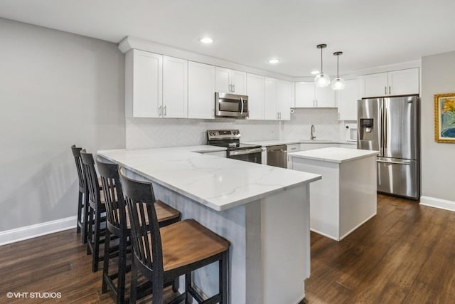 kitchen with a peninsula, baseboards, dark wood-style floors, a sink, and appliances with stainless steel finishes