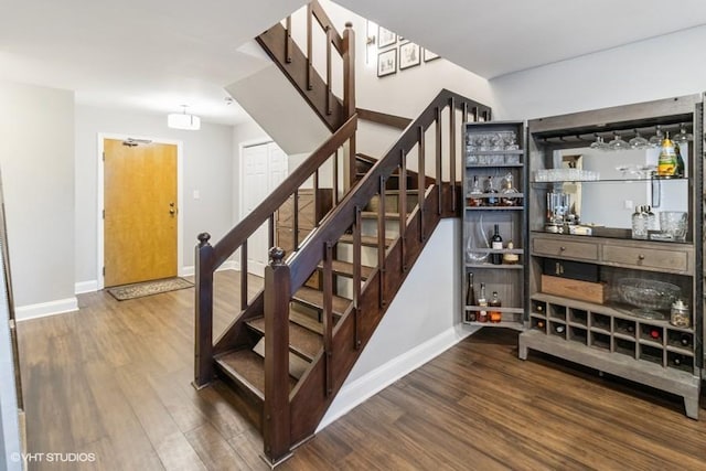 stairway with baseboards, a bar, and wood finished floors