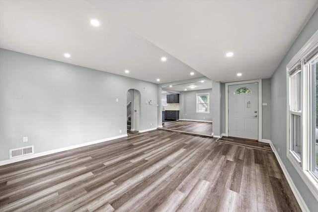 unfurnished living room featuring arched walkways, visible vents, wood finished floors, and recessed lighting