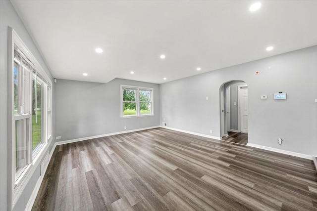 unfurnished living room with baseboards, arched walkways, and wood finished floors