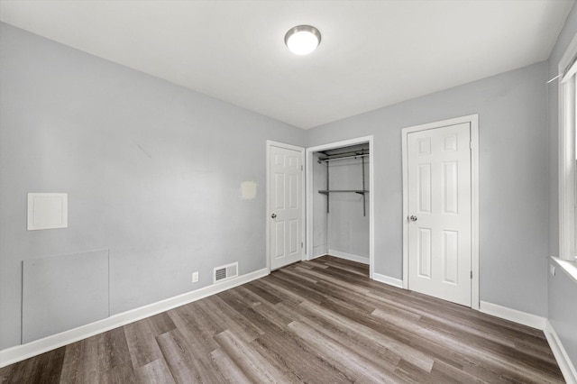 unfurnished bedroom featuring baseboards, a closet, wood finished floors, and visible vents