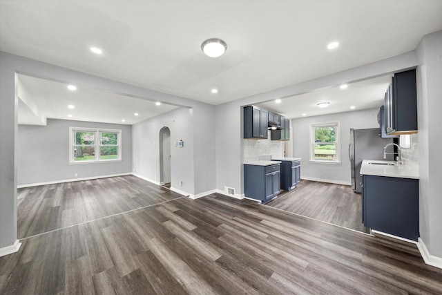 unfurnished living room with arched walkways, baseboards, dark wood finished floors, and plenty of natural light