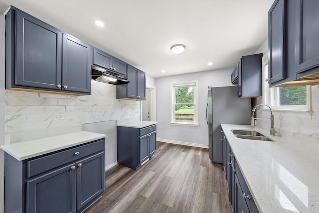 kitchen with light stone countertops, a sink, dark wood finished floors, tasteful backsplash, and under cabinet range hood