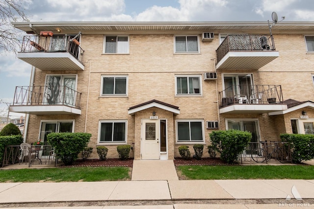 view of front facade with brick siding, a balcony, and a wall mounted air conditioner