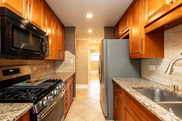 kitchen featuring light stone counters, a sink, stainless steel appliances, light tile patterned floors, and backsplash