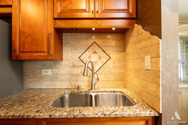 kitchen with a sink, light stone counters, decorative backsplash, and brown cabinetry
