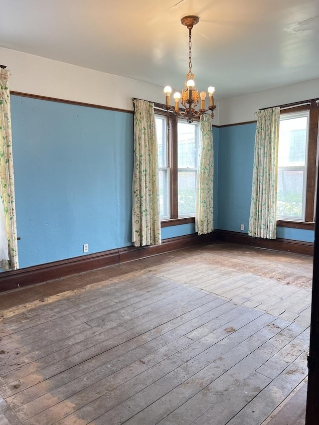 empty room with baseboards, a notable chandelier, and hardwood / wood-style flooring